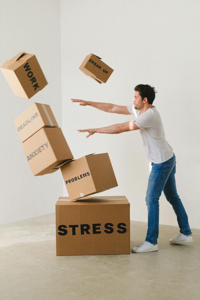 Man juggling boxes labeled with stressors like 'WORK' and 'DEADLINE,' illustrating the overwhelming nature of stress.