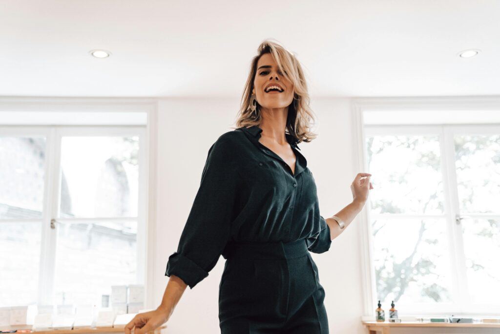 Confident, smiling woman in a black jumpsuit standing in a bright, modern office setting.