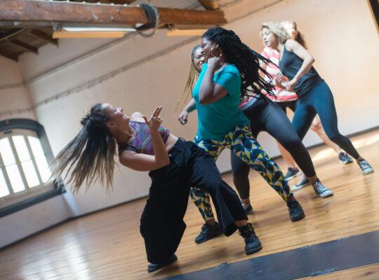 A diverse group of women of varying ages, sizes, and ethnicities dancing together in workout clothes.