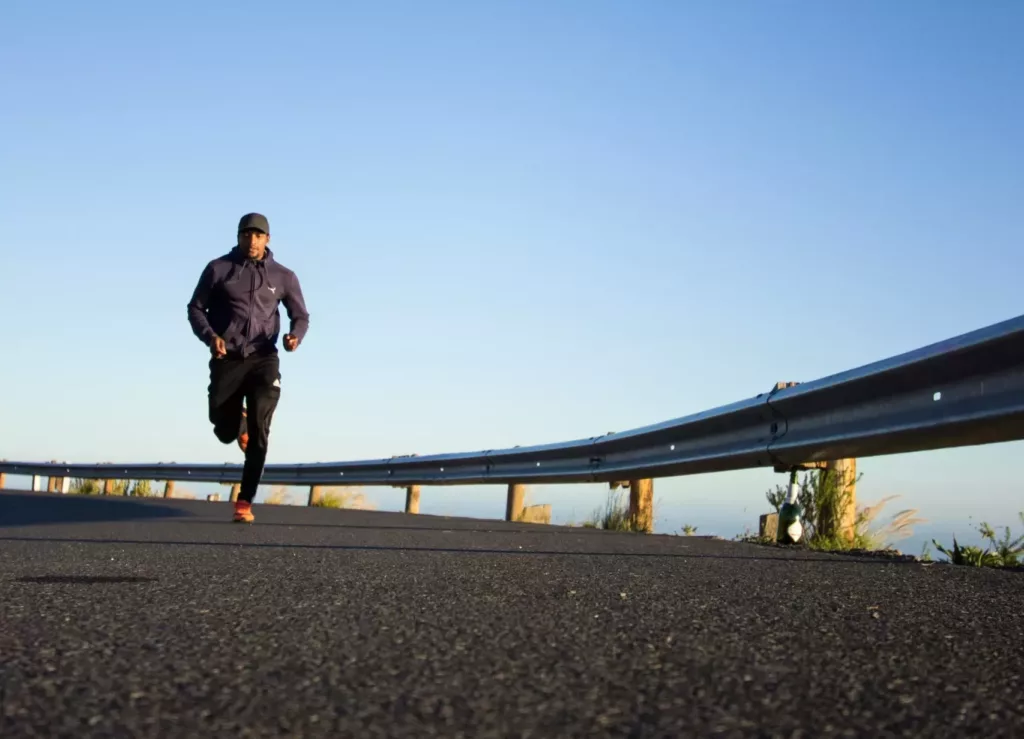 A black man in running attire strides towards the camera on a curved elevated roadway with a guardrail.